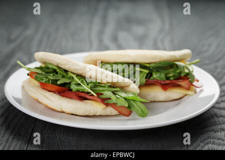 Deux sandwichs au jambon tomates et roquette dans le pain pita sur plaque, sur table en bois Banque D'Images
