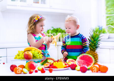 Heureux les petits enfants, mignon bébé fille et bébé garçon drôle, frère et soeur, manger des fruits mûrs pour petit-déjeuner sain Banque D'Images