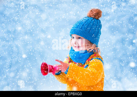 Fille adorable, mignon tout-petit dans un chapeau tricoté et yellow nordic chandail, jouer avec des jouets de Noël, flocons de neige de Bell Banque D'Images