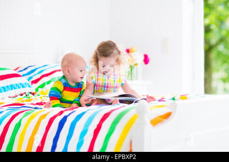 Deux enfants, curly peu bébé fille et bébé garçon drôle, frère et soeur, de lire un livre assis dans la chambre à coucher de soleil Banque D'Images