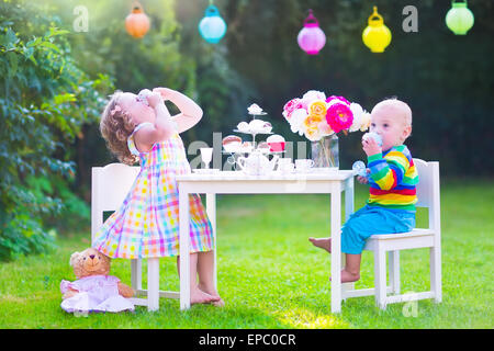 Deux enfants heureux, cute girl bouclés et un petit bébé garçon, frère et soeur, bénéficiant d'un thé avec leurs jouets Banque D'Images