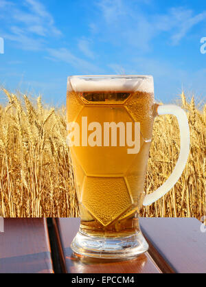 Verre de bière sur la table en bois contre les épis de blé d'or et bleu ciel. Banque D'Images