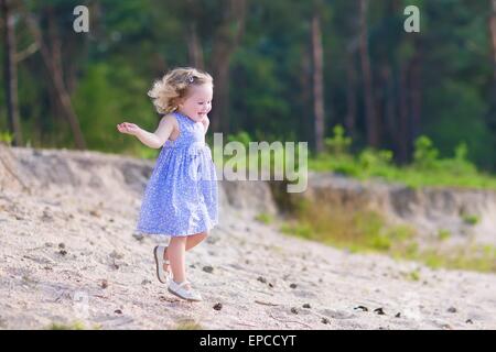 Adorable enfant, peu curly girl dans une robe d'été bleu tournant et jouant sur les dunes de sable dans la forêt de bois de pin Banque D'Images