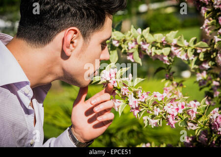 Beau jeune homme en odeur de belles fleurs dans le jardin d'une journée ensoleillée Banque D'Images