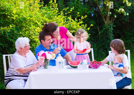 Grande famille heureux appréciant le déjeuner avec grand-mère manger des fruits, du melon et des fraises dans le jardin Banque D'Images