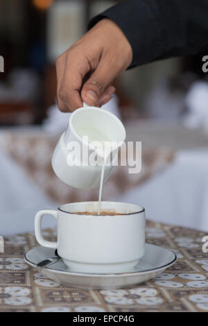 Garçon verse du lait dans une tasse de chocolat sur la table. Banque D'Images