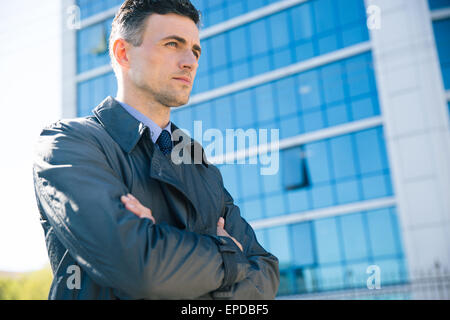 Portrait d'un confident businessman standing with arms folded extérieur. Bâtiment de verre sur fond de Banque D'Images