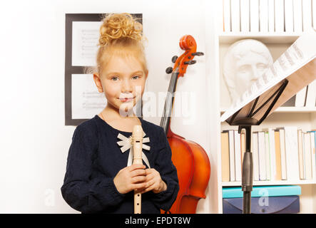 Cute blonde girl avec flûte debout près de violoncelle Banque D'Images