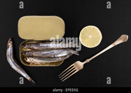 Anchois Frais de poisson avec de l'argent peuvent isolés de fourche sur fond texturé noir, vue du dessus. Manger des fruits de mer sains culinaire. Banque D'Images