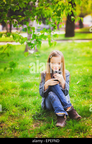 Portrait of smiling teenage girl sitting in park et des textos sms à l'aide de téléphone mobile Banque D'Images