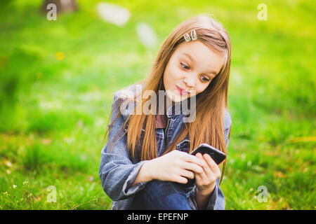 Portrait of smiling teenage girl sitting in park et des textos sms à l'aide de téléphone mobile Banque D'Images