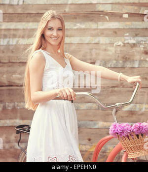 Belle blonde femme portant une jolie robe s'amusant en parc avec location portant un panier plein de belles fleurs de pivoine Banque D'Images