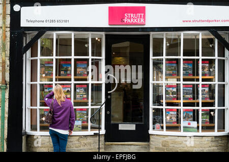 Une femme à la maison à des prix dans la fenêtre de Strutt et Parker estate agents Cirencester, Gloucestershire, Angleterre, Royaume-Uni Banque D'Images