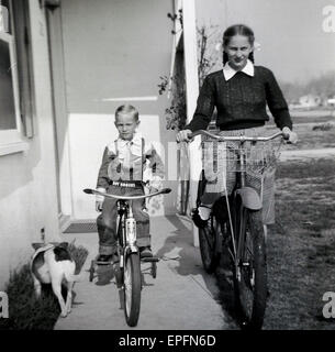 Années 1950, historiques, deux enfants, frère et soeur, s'asseoir sur leurs bicyclettes sur le porche à l'extérieur de leur maison dans le Mid-west, le petit garçon vêtu d'un costume Roy Rogers. Banque D'Images