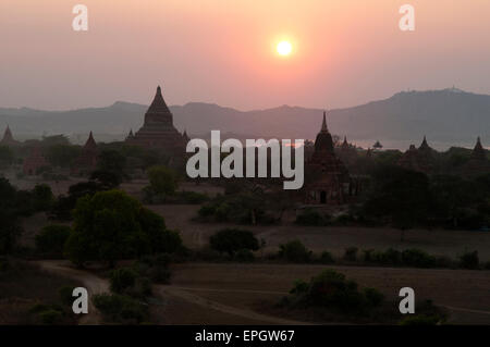 Les silhouettes sombres des temples en pierre contre la lueur jaune d'un coucher de soleil à Bagan Myanmar Banque D'Images