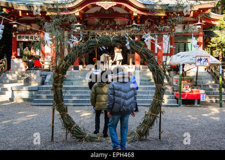 Japon, Nishinomiya, sanctuaire de Koshiki-wa. Un jeune couple entre dans le sanctuaire en marchant à travers un chi-no-wa, un cercle de corde torsadé mis en place pour la nouvelle année. Banque D'Images