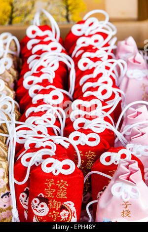 Rangées de breloques de bonne chance rouges et roses omamori avec des cordons de cravate blancs, empilées en rangées sur le comptoir d'un sanctuaire Shinto au Japon. Banque D'Images