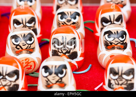 Gros plan de quatre rangées de visages de poupée de paper-maché rouge Daruma à vendre au temple de Suma-dera à Suma, Kobe. Ils représentent le visage d'un homme barbu. Banque D'Images