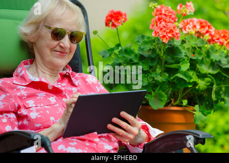Femme avec tablette, Young Senior à l'extérieur dans son jardin extérieur Lecture Happy Smiling Banque D'Images