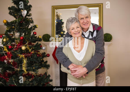 Senior couple hugging à côté de leur arbre de Noël Banque D'Images