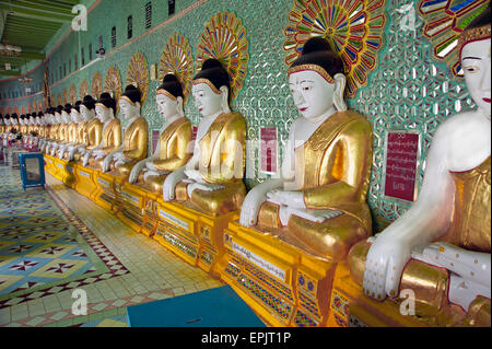 Longue rangée de Bouddhas en pierre peint contre un mur du temple vert dans l'ancienne capitale du Myanmar Sagaing Banque D'Images