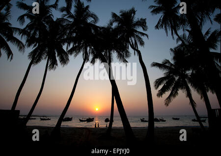 Trois figures et de palmiers se découpant contre le Ciel de coucher du soleil sur la plage de Ngapali Myanmar Banque D'Images