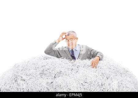 Portrait d'un homme mûr confus à la recherche de quelque chose dans une pile de papier déchiqueté isolé sur fond blanc Banque D'Images