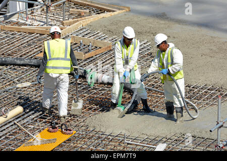 Gros plan sur le site de l'industrie de la construction de bâtiments des travailleurs occupés plaçant et faisant vibrer le béton de pompage dans le bloc d'appartements de dalle de plancher de renfort Londres Royaume-Uni Banque D'Images