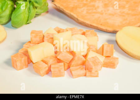 Dés de pommes de terre et la patate douce, en face des herbes et des légumes Banque D'Images