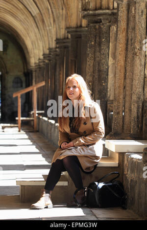 Jeune femme assise dans les cloîtres de Norwich Cathedral, Norwich, Norfolk, Royaume-Uni Banque D'Images