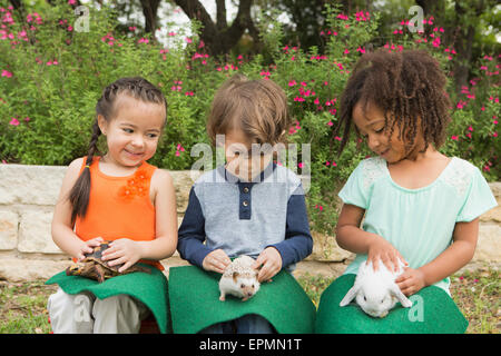 Trois enfants assis dans une rangée, chacun avec un petit animal sur leurs genoux. Banque D'Images