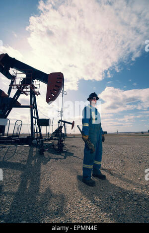 Un homme en bleu de travail et casque à une pompe à balancier en pleine terre à un site d'extraction d'huile.