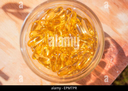 Omega 3 capsules dans un verre peut, sur une planche à découper en bois Banque D'Images