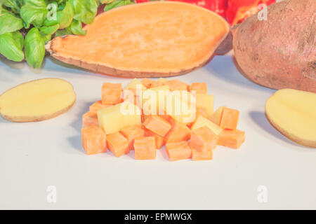 Dés de pommes de terre et de patates douces, en face des herbes et des légumes Banque D'Images