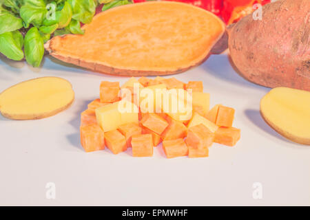 Dés de pommes de terre et de patates douces, en face des herbes et des légumes Banque D'Images