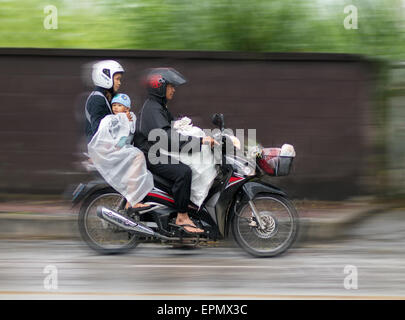 Balades en famille asiatique sous la pluie sur une moto Banque D'Images