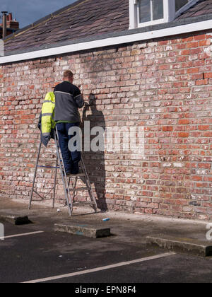 Workman avec un marteau et un ciseau à froid à des vieux râteau de mortier d'un mur de briques avant de revenir plus tard et se rendre Banque D'Images