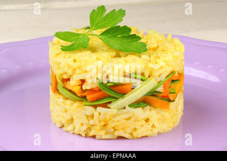 Riz safrané aux légumes croquants, les carottes et courgettes, décoré de persil, servis sur une plaque sur rose. Banque D'Images