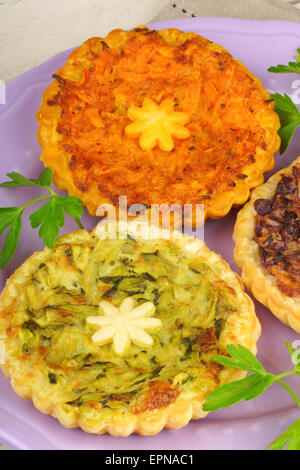 Trois mini quiches végétariennes avec un trevisano chicorée, l'un avec des carottes et une avec la courgette, servis sur une plaque sur une rose Banque D'Images