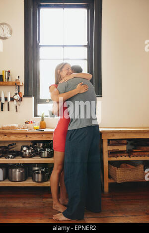 Tourné à l'intérieur du couple dans la cuisine. Image de l'homme pleine longueur hugging woman en matinée. Souhaitant bonne journée Banque D'Images