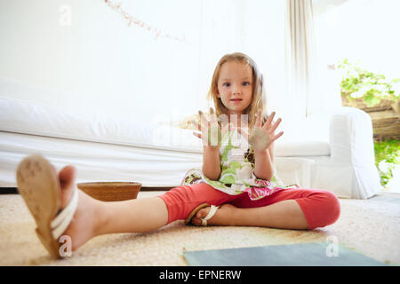 Portrait de belle petite fille s'amuser tout en peinture. Séance d'écolière sur le plancher à la maison montrant ses paumes. Banque D'Images