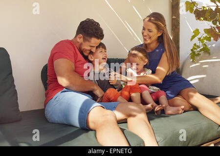 Photo de famille heureuse de quatre dans son jardin en s'amusant, assis sur la table de lecture. Les parents jouer avec les enfants rire dans patio Banque D'Images