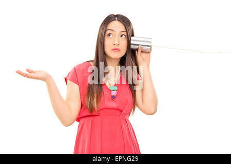 Jeune femme parlant confus par une boîte en fer-blanc et de téléphone des gestes avec sa main isolé sur fond blanc Banque D'Images