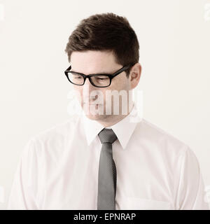 Portrait of businessman avec des lunettes, chemise blanche et cravate dans Office. Il est à la recherche vers le bas avec une expression grave. Banque D'Images