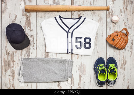 Tas de vêtements de sport et équipement de base-ball sur un plancher de bois blanc Banque D'Images