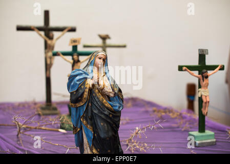Centro Cultural Convento San Francisco Statue de la Vierge Marie Grenade Nicaragua | GRANADA, Nicaragua — Une statue polychrome de la Vierge Marie se dresse parmi plusieurs crucifix au Centro Cultural Convento San Francisco, entourée de branches épineuses posées sur un tissu violet marquant les dévotions du Carême. L'ancien couvent franciscain, fondé en 1529, conserve des artefacts religieux de l'ère coloniale que les moines espagnols utilisaient autrefois comme outils pédagogiques visuels pour introduire les récits catholiques en Amérique centrale. Banque D'Images