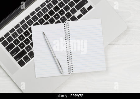 Portrait de l'ordinateur portable et le bloc-notes avec stylo argent blanc sur blanc rustique bureau. Banque D'Images