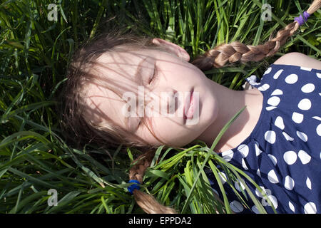 Jolie jeune fille de race blanche avec deux tresses de cochon couché et dormir sur l'herbe verte Banque D'Images