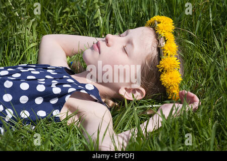 Young pretty caucasian girl en pissenlits jaunes garland couché et dormir sur l'herbe verte Banque D'Images