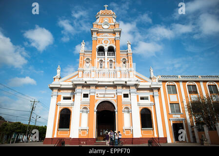 Iglesia De Xalteva Tour baroque orange et blanche Granada Nicaragua | GRANADA, Nicaragua — Les visiteurs se rassemblent à l'entrée de l'Iglesia de Xalteva sous sa façade baroque orange et blanche, couronnée d'un clocher portant un monogramme Chi Rho. L'église sert le quartier de Xalteva, la colonie indigène qui a précédé la fondation espagnole de Granada en 1524 ; sa façade a été reconstruite entre 1895 et 1898 après un tremblement de terre survenu en 1890, les travaux de décoration étant achevés en 1921. Banque D'Images